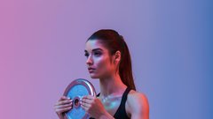 Photo of beautiful strong young sports woman make exercises with gym barbell disk isolated over purple wall background. Looking aside.