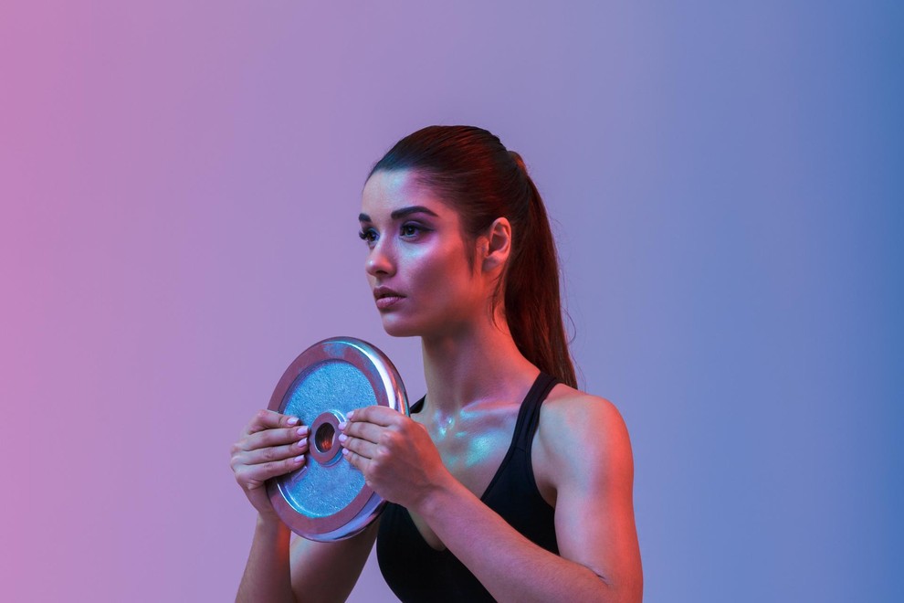 Photo of beautiful strong young sports woman make exercises with gym barbell disk isolated over purple wall background. Looking aside.
